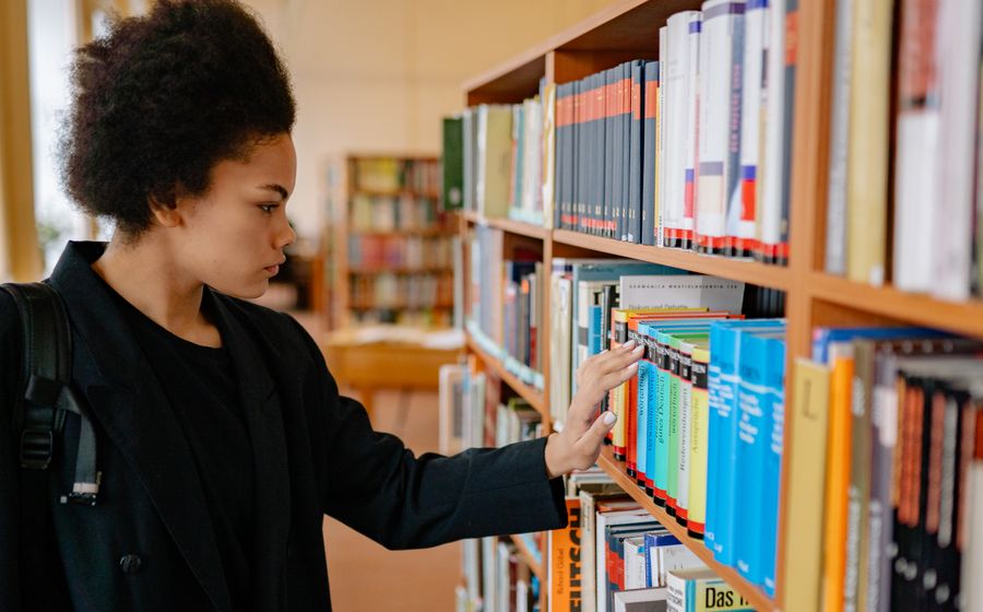Étudiante hésitante devant les rayons d'une bibliothèque